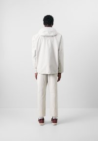 Lätt vit jacka med huva, i kombination med matchande lätta byxor, med en avslappnad passform och subtil textur. Bruna sneakers ingår.