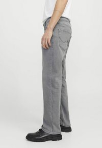 Jean en denim gris avec un coupe droite, design à cinq poches et détails de couture subtils, associés à des chaussures noires à lacets.