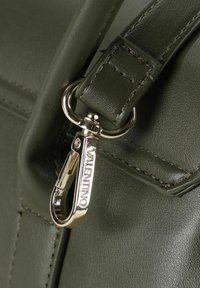 Conector de correa para bolso de cuero verde oscuro con herrajes plateados y la palabra "VALENTINO" grabada en el clip. Textura lisa y costuras visibles.