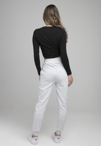 Black cropped long-sleeve top paired with gray sweatpants. Pants feature elastic waistband and tapered legs. Model wears white sneakers.