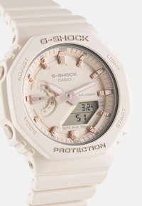 G-SHOCK watch with a cream silicone strap, octagonal case, light rose gold details, digital screen, and analog sub-dial for timekeeping.