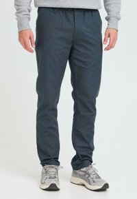 Mørkeblå bukser med elastisk liv, skrå sidelommer, i et teksturert stoff og med avsmalnende ben. Brukes med grå joggesko.