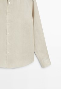 Beige long-sleeve button-up shirt with a straight hem and buttons down the front, displayed against a white background.