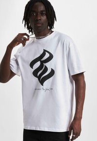 Balta medvilninė marškinėlių su dideliu juodu grafiku, kuriame yra stilizuotos raidės "B" ir "W", ir užrašas "ESTABLISHED New York 1999" spausdinamas žemiau.