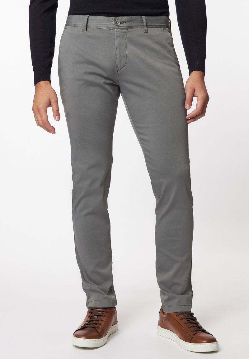 Graue Baumwollhose im Slim-Fit mit detaillierten Nähten, Vordertaschen und Knopfverschluss, getragen mit braunen Sneakern mit weißen Sohlen.