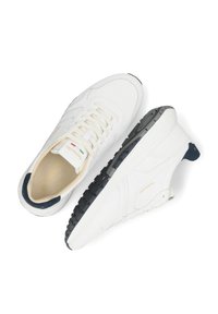 Baskets blanches en cuir avec une surface texturée, dotées d'une semelle en caoutchouc épaisse, de lacets crème et d'un accent bleu marine au niveau du talon. Détail du logo doré à l'intérieur.