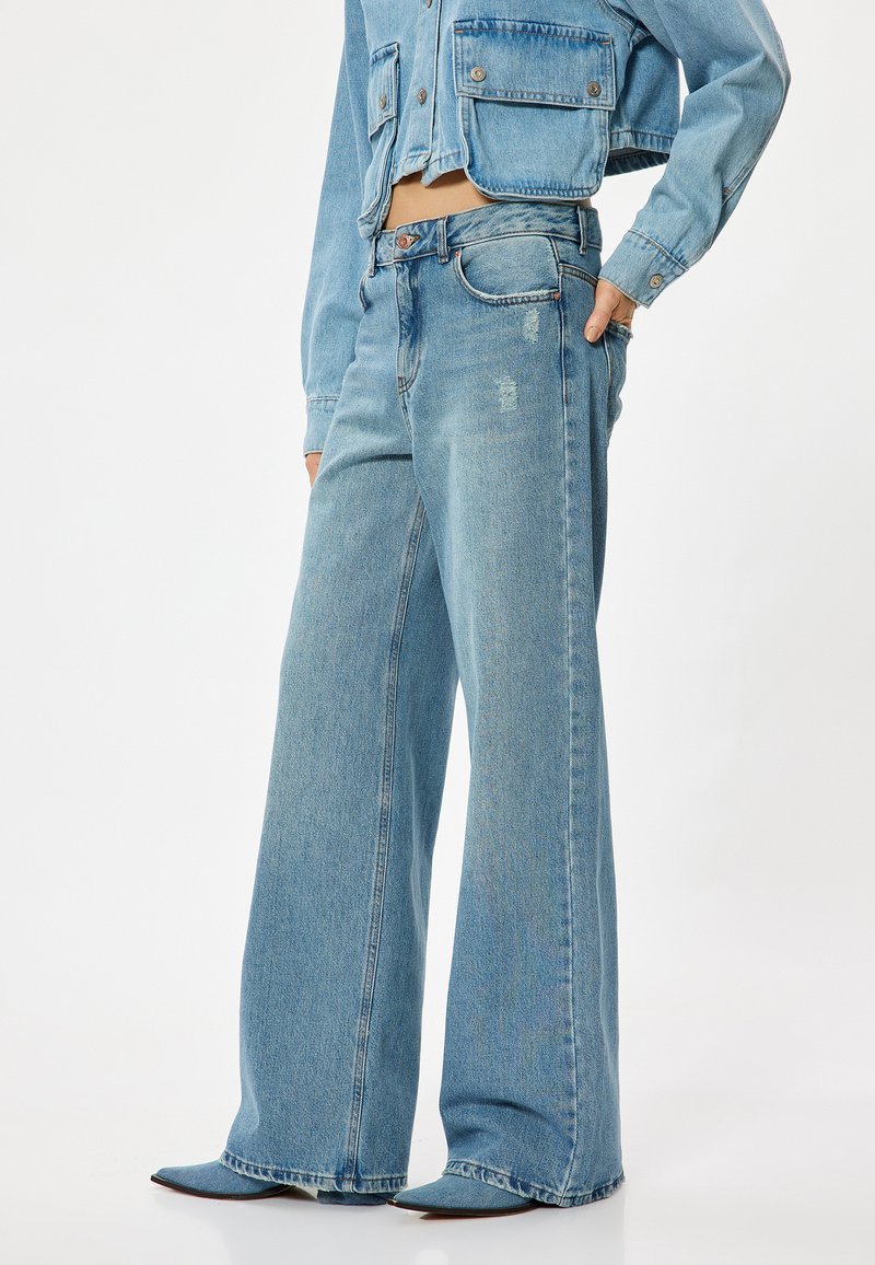 Ljust blå vida jeans i denim med en urblekt finish och subtila slitningar, kombinerade med en matchande kort denimjacka.