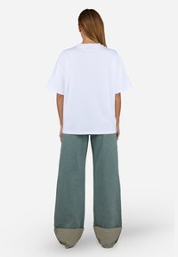 T-shirt oversize blanc associé à un pantalon en denim vert à jambes larges, avec un ourlet beige contrastant. Design simple avec une texture douce.