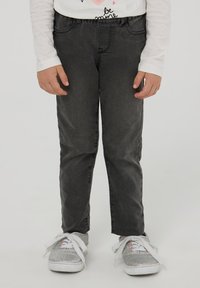 Czarne dżinsy w wąskim kroju z delikatnym połyskiem, zestawione z srebrnymi sneakersami z białymi sznurowadłami i różowymi akcentami.