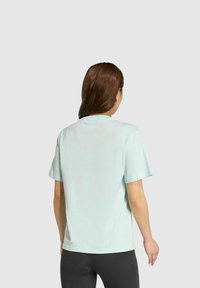 Camiseta de manga corta en azul claro, hecha de una tela suave. Presenta un cuello redondo clásico y un corte relajado, vista desde la parte posterior.