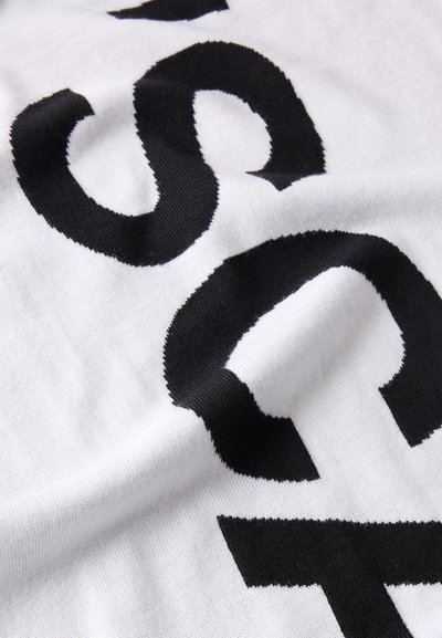 Tissu blanc avec de grandes lettres noires audacieuses imprimées, montrant un gros plan des parties courbes et droites du texte sur un textile doux.