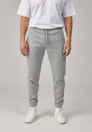 Light grey cotton sweatpants feature a tapered fit, drawstring waistband, and ribbed cuffs, paired with white sneakers.