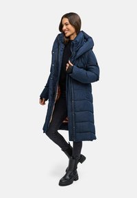 Donkerblauwe gewatteerde jas met een lange snit, een oversized capuchon en drukknoopsluitingen. Kenmerkt zich door een geborduurde textuur en een warm gevoerd interieur.
