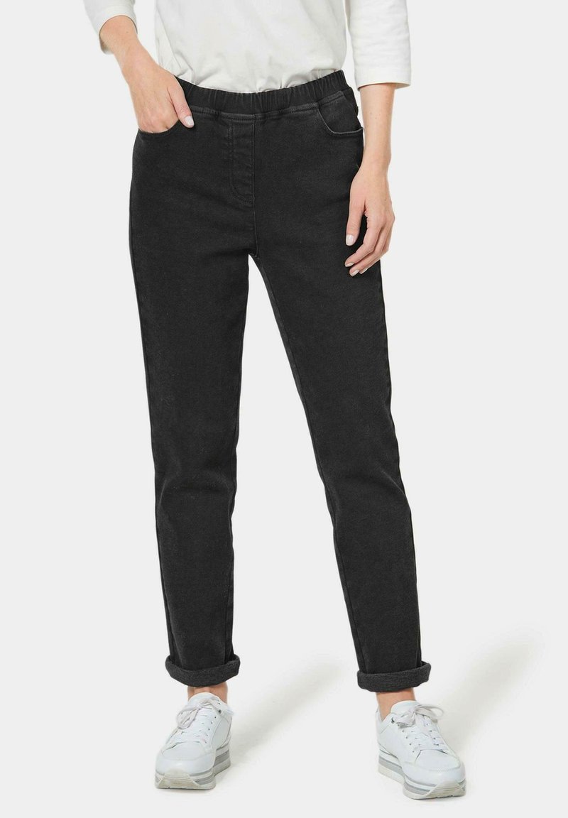 Joggers en denim noir avec une taille élastique, deux poches avant, des poignets retroussés et une coupe ajustée, associés à des chaussures de sport blanches.