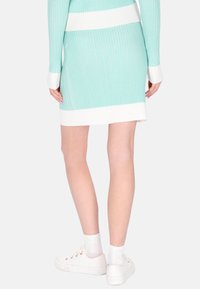 Zöldessárga-fehér vízszintes csíkozású bordázott kötött ruha. A ruhának hosszú ujjai és testhezálló sziluettje van, fehér tornacipővel párosítva.