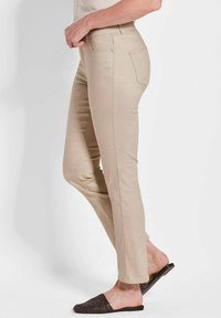 Beige, strukturierte Slim-Fit-Hosen mit glatter Oberfläche und Gesäßtaschen, kombiniert mit einem hellen Oberteil und einer schwarzen, gewebten Rutschsandalette.