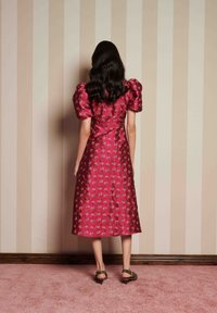 Um vestido de comprimento médio, com mangas bufantes, em cetim rosa brilhante com bordados florais. Apresenta um corpete ajustado e uma saia rodada.