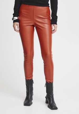 Pantalons en simili cuir orange, taille haute et ajustés, avec une texture lisse, assortis à des bottines noires à détails zippés.