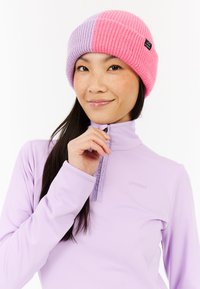 Pletená čiapka s ružovými a levanduľovými pruhmi, rebrovanou textúrou a malou čiernou logom nášivkou. Nosená s svetlo purpurovým zipsovým topom.