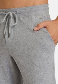 Grijze sweatpants met een geribbelde tailleband en koord. Voorzien van zijzakken en een klein logo detail nabij de tailleband. Zachte textuur.