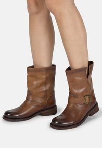 Bottines en cuir marron avec une accent de boucle, un petit talon empilé, et un dessus flasque avec une finition texturée.