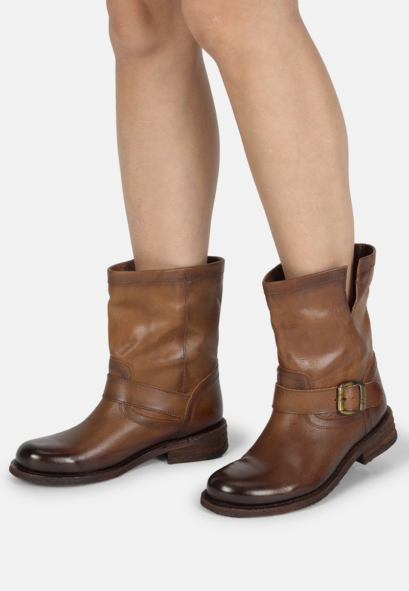 Bottines en cuir marron avec une accent de boucle, un petit talon empilé, et un dessus flasque avec une finition texturée.