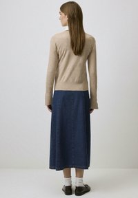 Beige lange mouw trui gecombineerd met een marineblauwe denim maxi rok. De rok heeft een rechte snit en een naad in het midden. Bruine schoenen maken de look compleet.