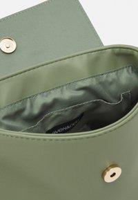 Borsa a tracolla in ecopelle verde con chiusura a scatto dorata. Interno con fodera in tessuto liscio ed etichetta del marchio. Design angolare e strutturato.