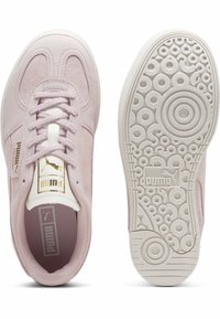 Lichtroze suède sneakers met witte rubberen zolen, voorzien van een vetersluiting, gouden details op de tong en een cirkelvormig profielpatroon.