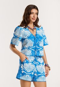 Zils zīmējuma komplekts ar baltām čaulu motīviem. Īsām piedurknēm ar dziļu izgriezumu un saskaņoti īsie šorti ar elastīgu jostu.