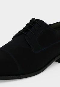 Chaussure Oxford formelle noire avec laçage fermé, bout droit et semelle en cuir lisse sur fond blanc.