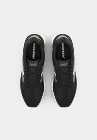 Black athletic shoes with a textured fabric upper, grey stripes, and white rubber sole. Features flat laces and brand logo on the tongue.
