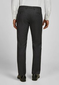 Donkergrijze dresspants met een subtiele textuur, slim fit en twee achterzakken. Gedragen met een wit shirt en zwarte schoenen.