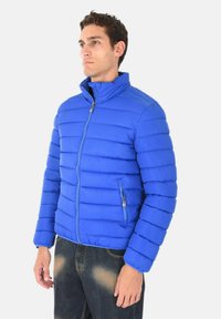 Giacca blu imbottita con cuciture orizzontali, colletto alto, zip frontale completa e tasche laterali. Realizzata in tessuto morbido e leggero.