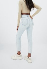 Jeans de tiro alto en azul claro con un ajuste slim, que presentan un diseño de bolsillo trasero y una etiqueta de cuero marrón en la cintura.