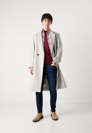 Cappotto grigio in lana, camicia a quadri, maglione bordeaux, jeans scuri, stivali Chelsea beige. Texture liscia, vestibilità su misura, dettaglio con un unico bottone.