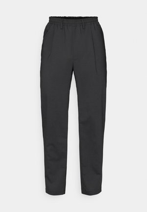 Black tapered trousers made from a smooth material. Feature a wide elastic waistband and two front pleats, with a simple design and no visible hardware.