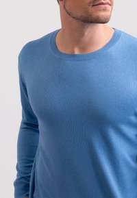 Hellblauer Strickpullover mit klassischem Rundhalsausschnitt, langen Ärmeln und glattem Material, ausgestattet mit dezenten Nähten an den Bündchen und am Saum.