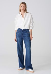 Chemise blanche légère à boutons, jean bleu à jambes larges et baskets blanches. Les jeans ont un design classique à cinq poches et une légère décoloration.