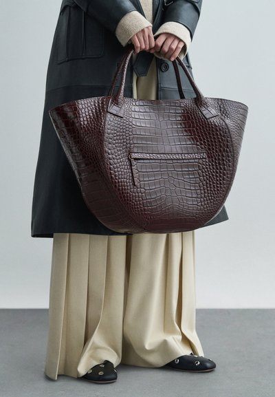 Μεγάλη σακούλα σε μπορντό χρώμα με σχέδιο κροκό, με διπλές λαβές και μπροστινή τσέπη με φερμουάρ. Λείος υφασμάτινος σχεδιασμός και ευρεία, στρογγυλή μορφή.