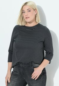 Schwarz-weiß gestreiftes Langarmshirt mit Rundhalsausschnitt, kombiniert mit dunklen Jeans, die mit Nietenakzenten an der Tasche versehen sind.