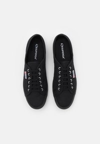 Mustat kangaskengät, joissa on pyöreä kärki, metalliset nauhakuulat, litteät nauhat, kumipohja ja pieni logo sivussa.