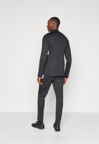 Schwarzes Langarmoberteil und passende Slim-Fit-Hose aus glattem Material, mit einem schlichten Design. Styling mit Sportschuhen.
