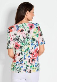 Blumen Kurzarmhemd mit einem hellrosa Hintergrund, das lebendige rote, blaue und grüne Muster zeigt. Weicher Stoff mit lässiger Passform.