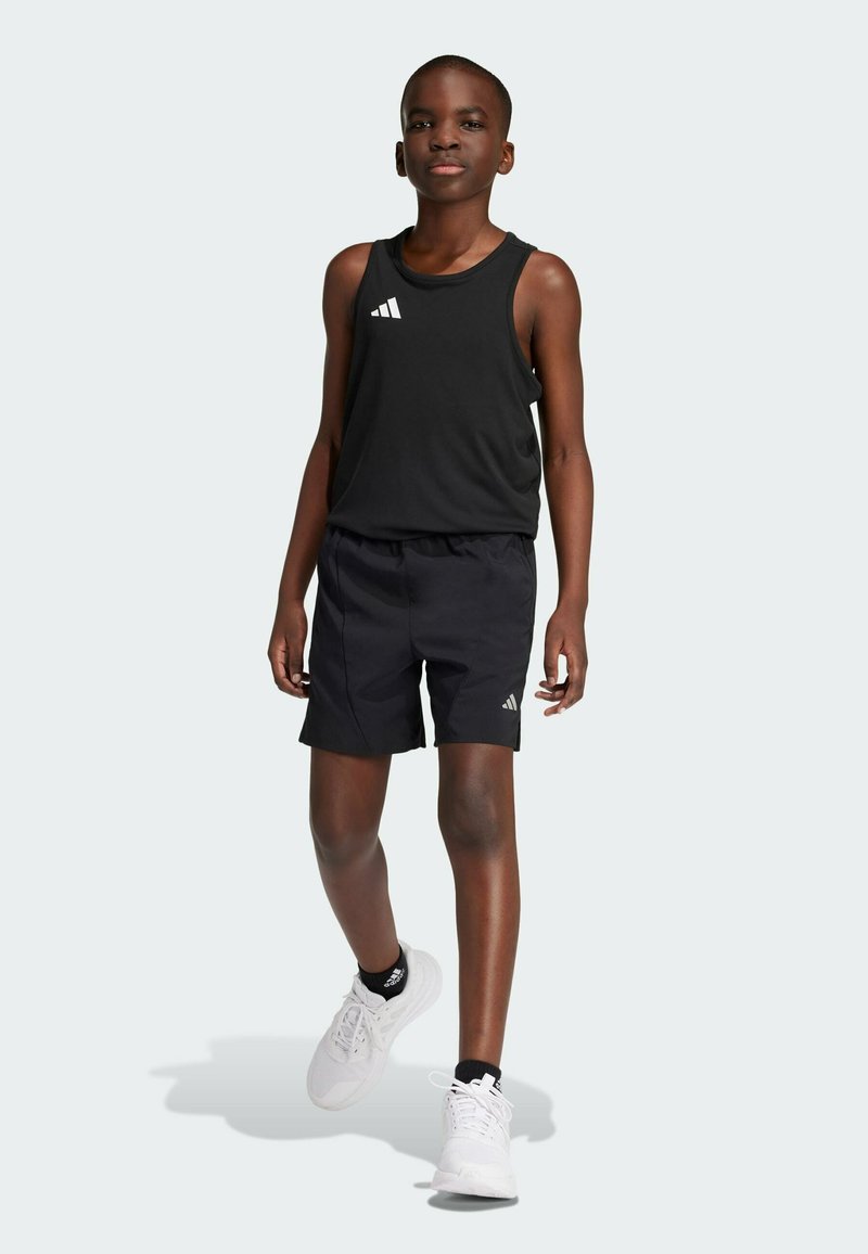 Top atlético negro sin mangas con logotipo blanco, combinado con pantalones cortos negros. Usado con zapatillas deportivas blancas con detalles en negro.