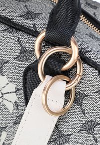 Borsa a mano in tessuto nero e bianco con texture, caratterizzata da motivi floreali, hardware in tonalità oro e anelli metallici doppi con un accento in pelle bianca.
