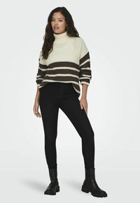 Maglione a collo alto a righe in crema e marrone, texture a coste, vestibilità over, abbinato a jeans skinny neri e stivaletti neri.