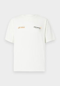 Λευκό βαμβακερό μπλουζάκι με κοντά μανίκια, με τη γραφή "Aston Martin" σε πορτοκαλί και το λογότυπο "McLaren" σε μαύρο, τοποθετημένο στο αριστερό στήθος.