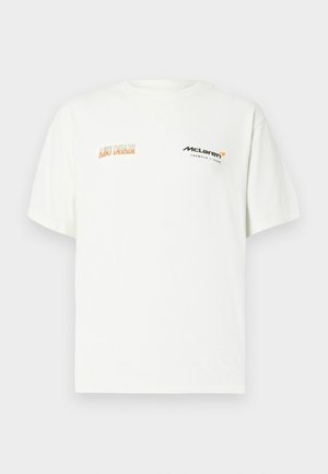 White cotton t-shirt with short sleeves, featuring "Aston Martin" in orange and "McLaren" logo in black, positioned on the left chest.