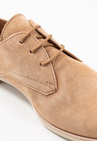 Tan nubuck leren schoen met een spitse neus, vetersluiting en subtiele stikdetails langs de bovenrand.